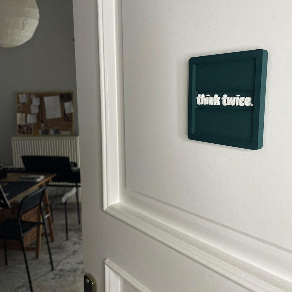 3D printed σουβέρ γραφείου “think twice.” σε πράσινο Morandi με λευκά ανάγλυφα γράμματα, που χρησιμοποιείται και ως διακοσμητικό τοίχου για home office.
