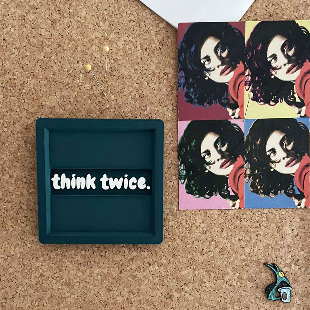 D printed σουβέρ “think twice.” σε πράσινο Morandi με λευκά ανάγλυφα γράμματα σε πίνακα ανακοινώσεων γραφείου, ως διακοσμητικό κάδρο.